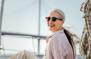 Woman with long gray hair in sunglasses smiling on a boat